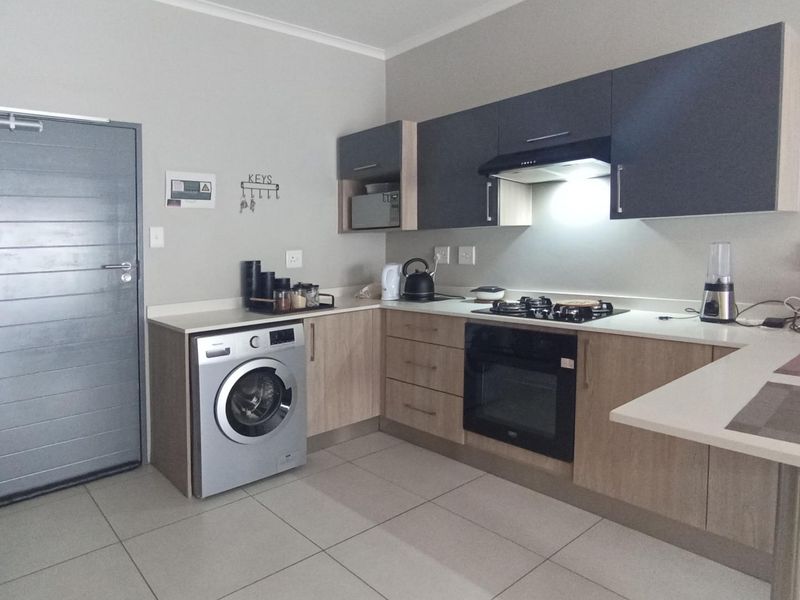 Modern kitchen featuring two-tone cabinetry, stone countertops, built-in gas hob, electric oven, extractor fan, and dedicated space for a washing machine.