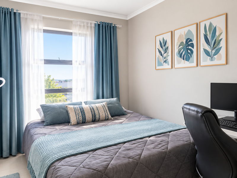 A well-maintained bedroom featuring neutral walls, tiled flooring, and an aluminium-framed window with integrated curtain tracks.
