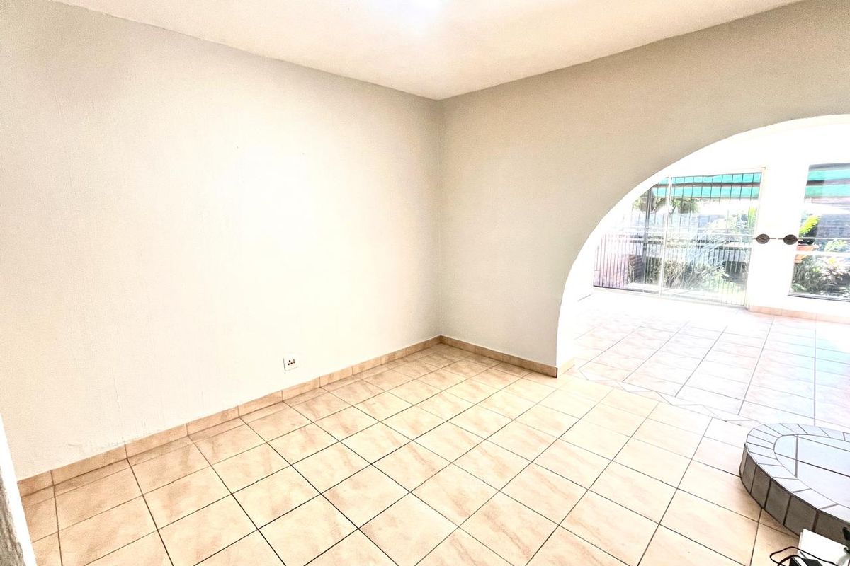 An empty living area featuring ceramic floor tiles and a distinctive arched doorway leading to an outdoor patio space.