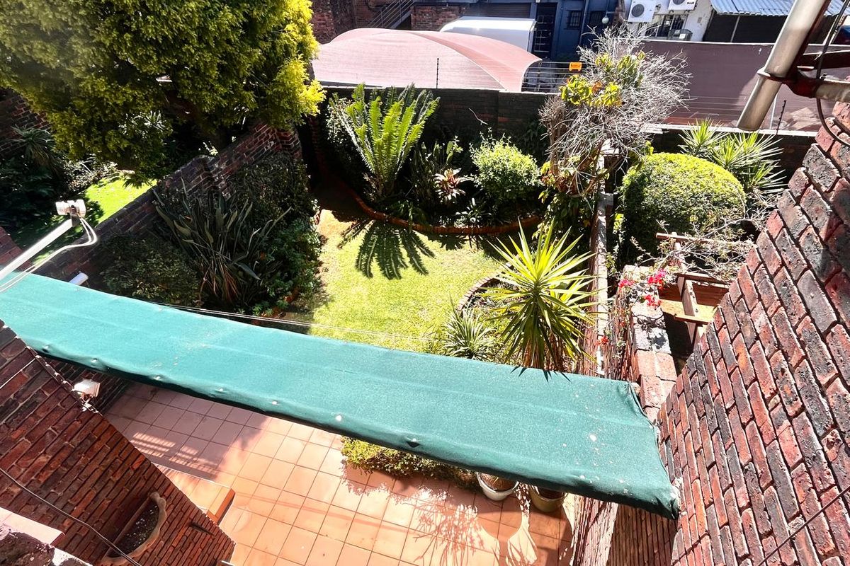 An elevated view of a private rear courtyard featuring a tiled patio area, a retractable awning, and a landscaped garden enclosed by brick walls.