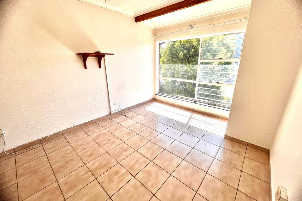 An empty bedroom featuring tiled flooring, a large window with natural light, and an exposed ceiling beam, ready for renovation or staging.
