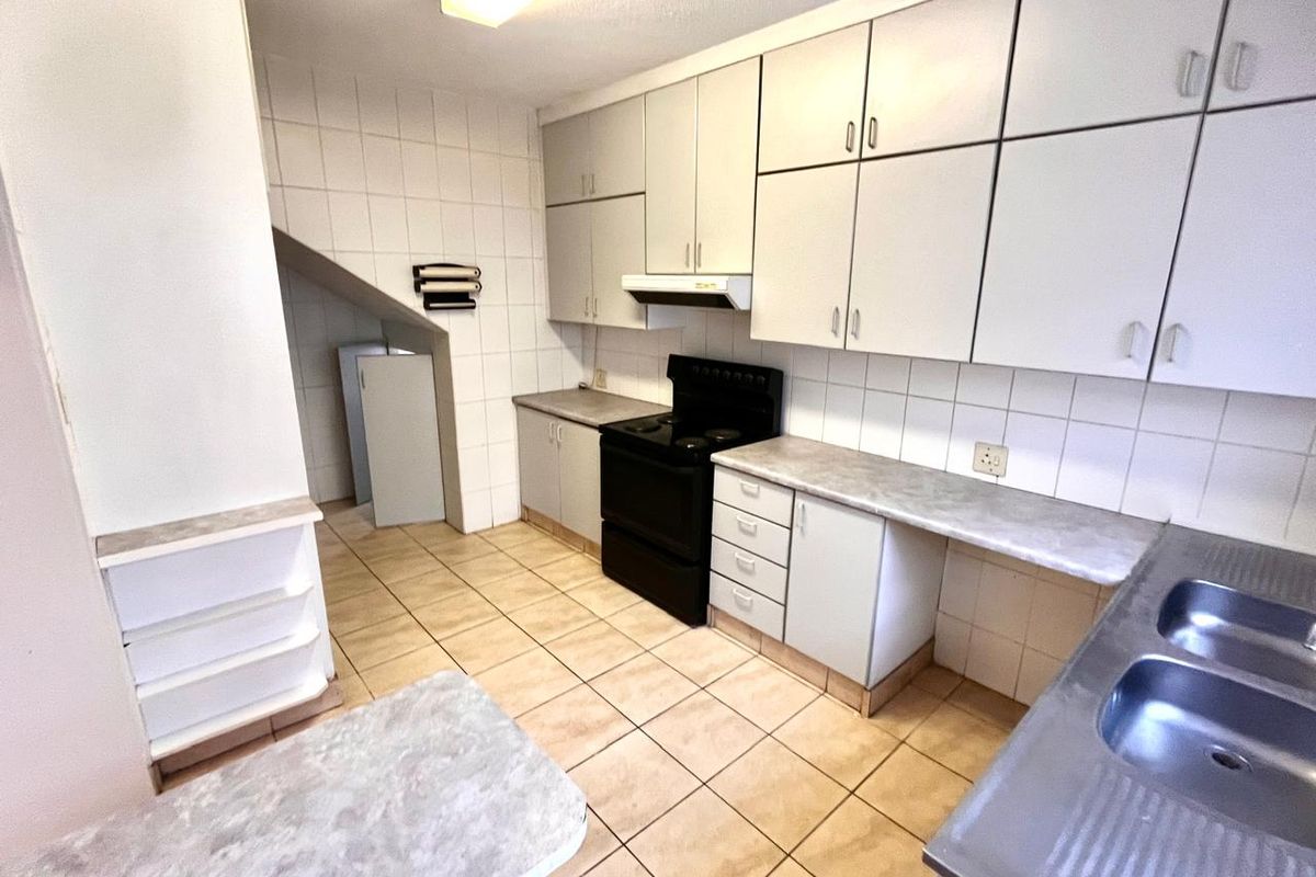 A functional kitchen featuring built-in cabinetry, laminate countertops, a double stainless steel sink, and a freestanding stove with an extractor fan.
