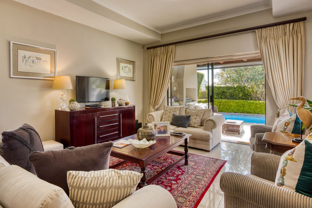 A well-maintained living room featuring tiled floors, recessed ceiling details, and large sliding glass doors providing seamless access to the outdoor pool area.