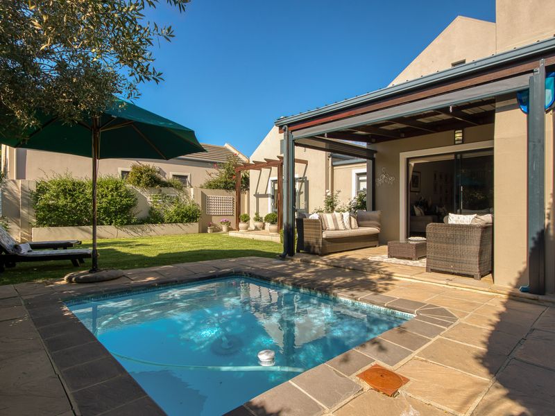 A well-maintained rear garden featuring a swimming pool, stone-paved surround, and a covered patio area with direct access to the home.