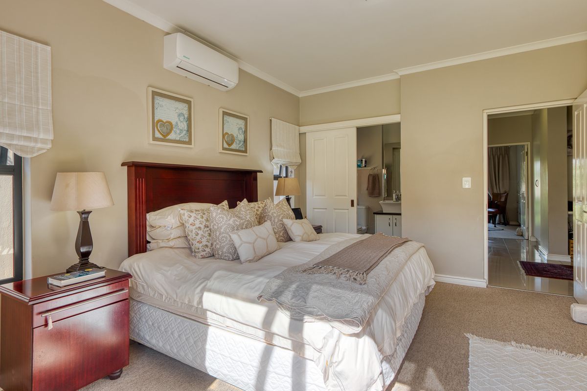A well-maintained bedroom featuring neutral wall tones, carpeted flooring, a wall-mounted air conditioning unit, and direct access to an en-suite bathroom.