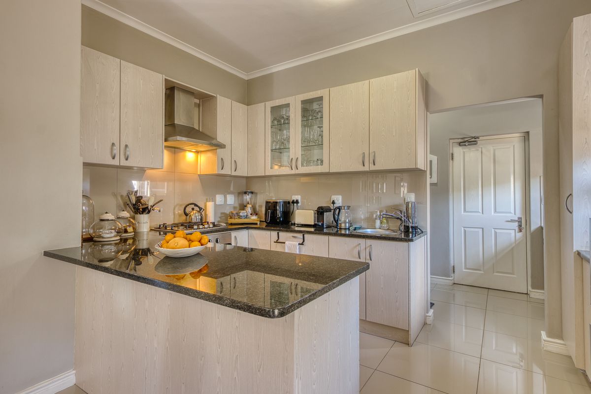 Modern kitchen featuring light wood-grain cabinetry, dark granite countertops, a gas hob with extractor fan, and polished floor tiles.