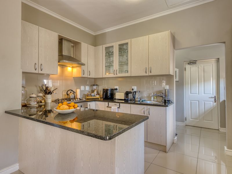 Modern kitchen featuring light wood-grain cabinetry, dark granite countertops, a gas hob with extractor fan, and polished floor tiles.