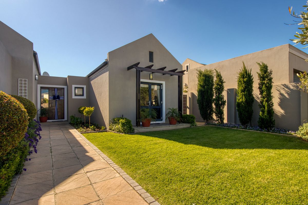 A well-maintained rear garden featuring a paved walkway, manicured lawn, and a timber pergola over the entrance to the home.