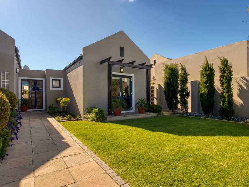 A well-maintained rear garden featuring a paved walkway, manicured lawn, and a timber pergola over the entrance to the home.