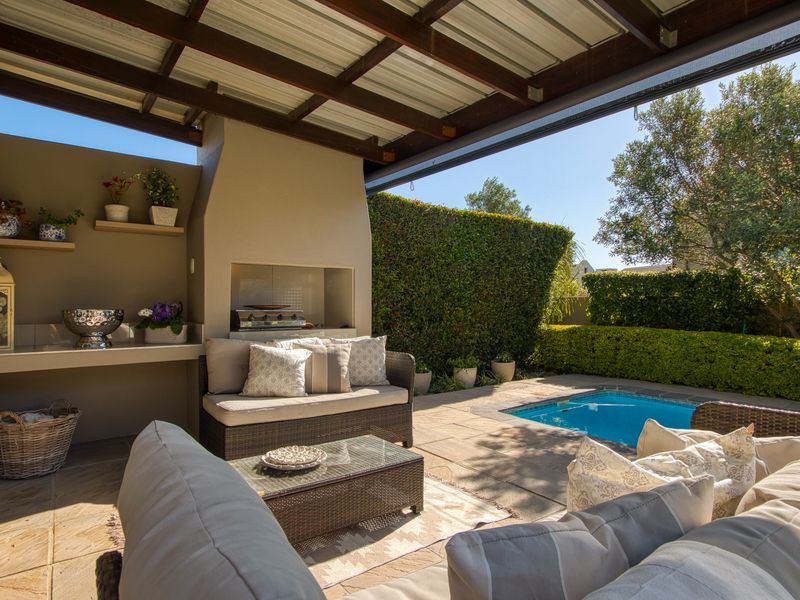 Covered outdoor patio featuring a built-in braai, stone flooring, and direct access to a private swimming pool and landscaped garden area.