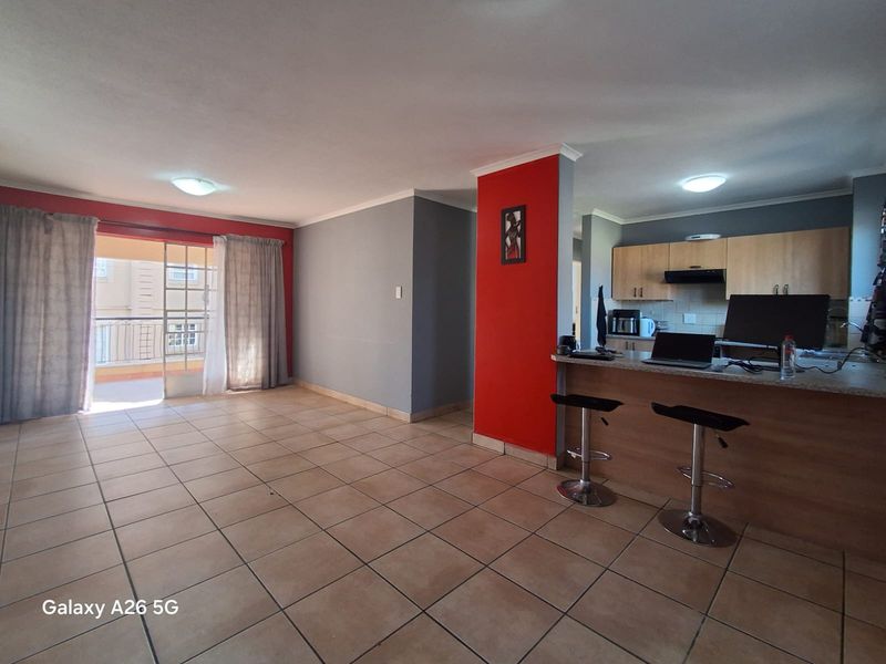 Open-plan living area featuring tiled floors, a breakfast bar, and a functional kitchen, with direct access to a balcony through sliding glass doors.