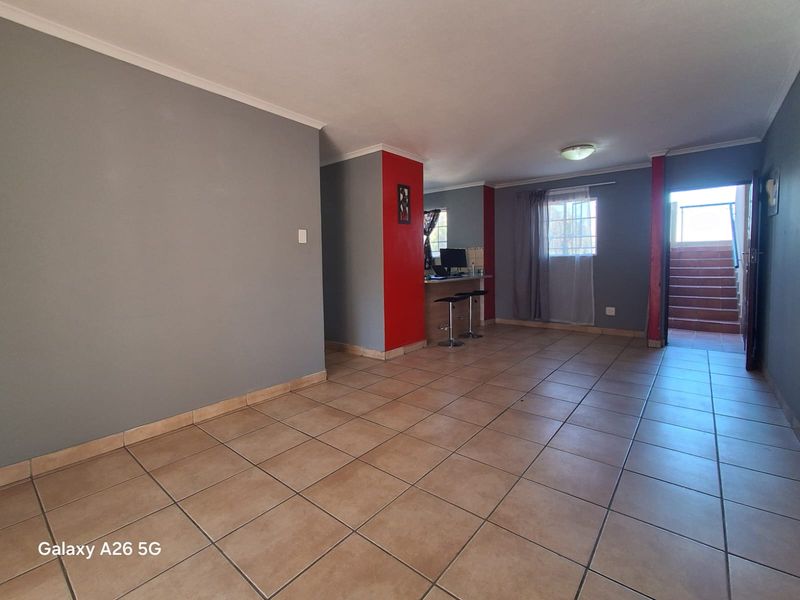 Spacious open-plan living area featuring tiled flooring, a breakfast bar, and direct access to an internal staircase.