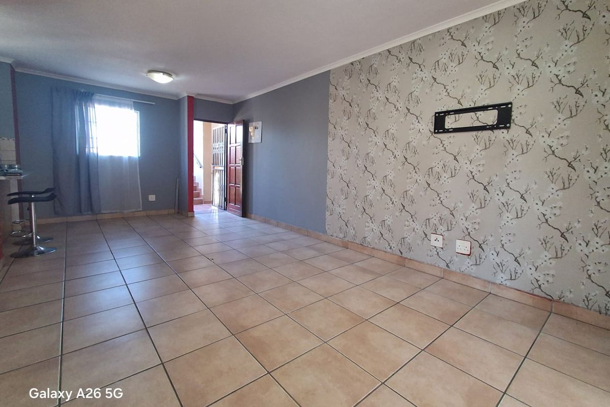 Spacious living area featuring ceramic floor tiles, a decorative wallpaper feature wall with a TV mount, and neutral grey painted walls.