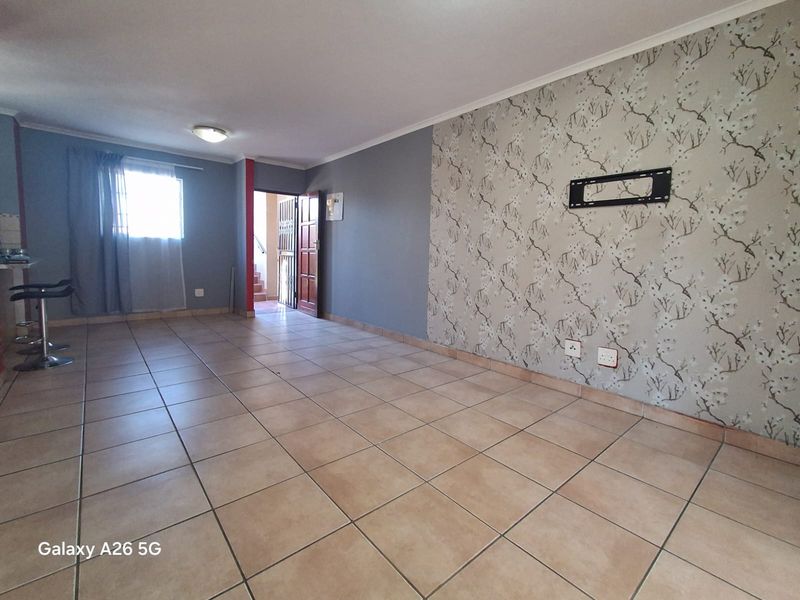 Spacious living area featuring ceramic floor tiles, a decorative wallpaper feature wall with a TV mount, and neutral grey painted walls.