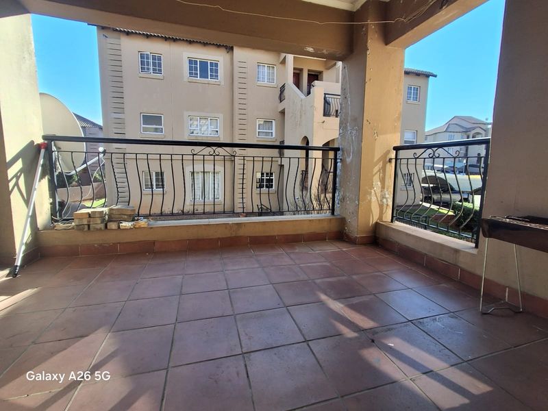 A covered balcony featuring tiled flooring and wrought iron railings, offering an outdoor space with views of the surrounding townhouse complex.