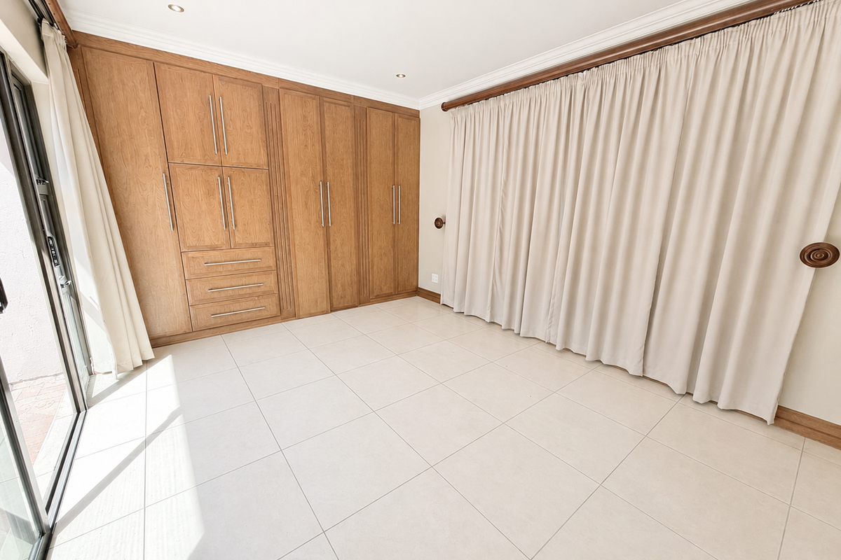 A bright, empty bedroom featuring extensive built-in wooden cabinetry, large format floor tiles, and a sliding glass door providing access to the exterior.