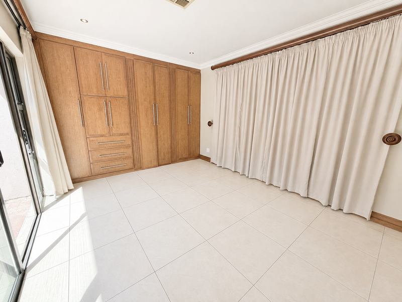 A bright, empty bedroom featuring extensive built-in wooden cabinetry, large format floor tiles, and a sliding glass door providing access to the exterior.