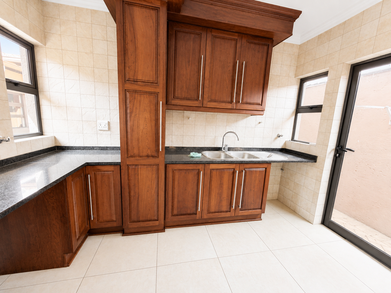 A clean and functional scullery featuring dark wood cabinetry, granite countertops, a double stainless steel sink, and direct access to the exterior.
