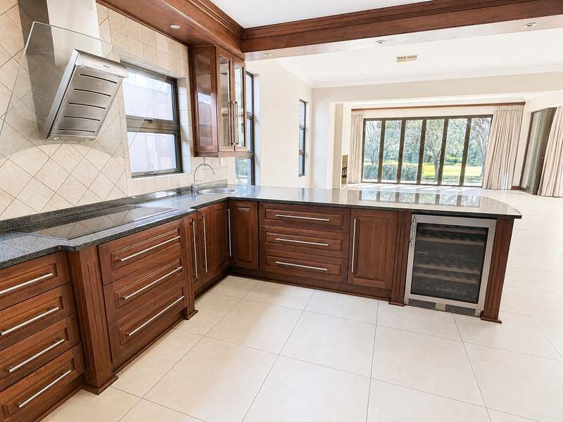 Spacious open-plan kitchen featuring rich wooden cabinetry, granite countertops, integrated wine cooler, and seamless flow to the living area with large glass sliding doors.