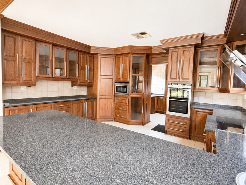 Spacious kitchen featuring extensive wooden cabinetry, granite countertops, a large central island, and integrated appliances including a built-in oven and microwave.