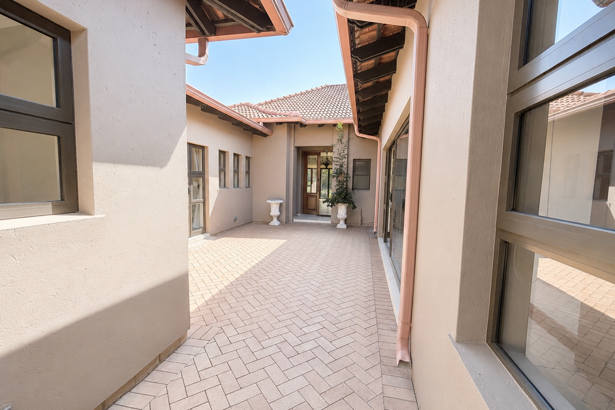 A well-maintained paved courtyard area featuring herringbone brickwork, aluminium window frames, and a covered entrance leading into the home.
