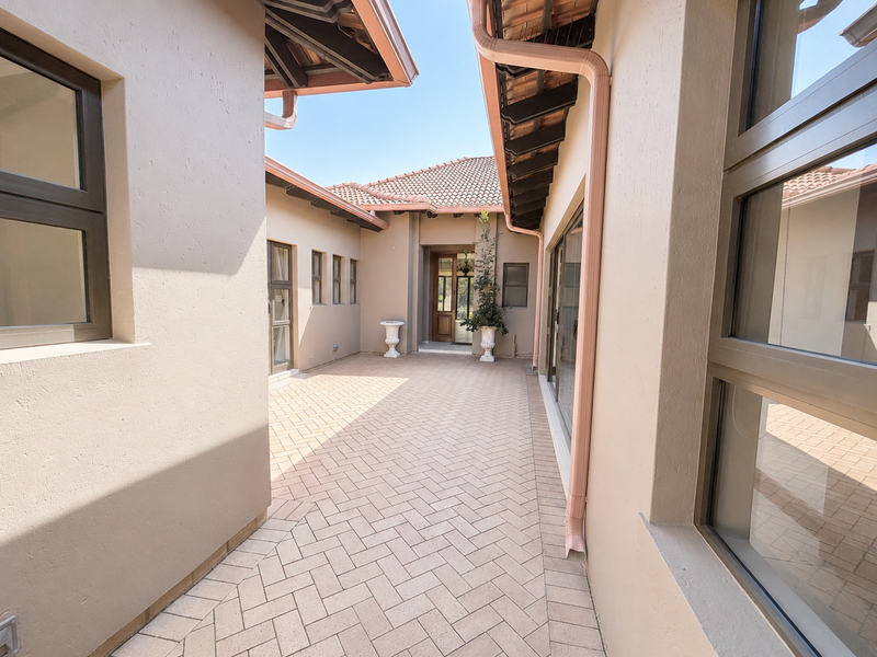 A well-maintained paved courtyard area featuring herringbone brickwork, aluminium window frames, and a covered entrance leading into the home.