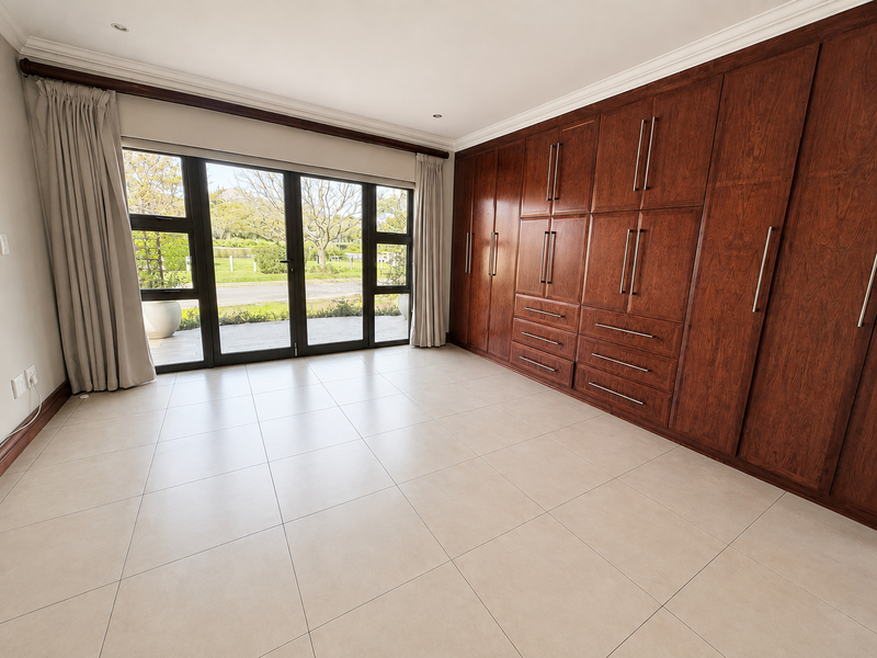 Spacious bedroom featuring extensive built-in wooden cabinetry, large sliding glass doors providing garden access, and neutral tiled flooring.
