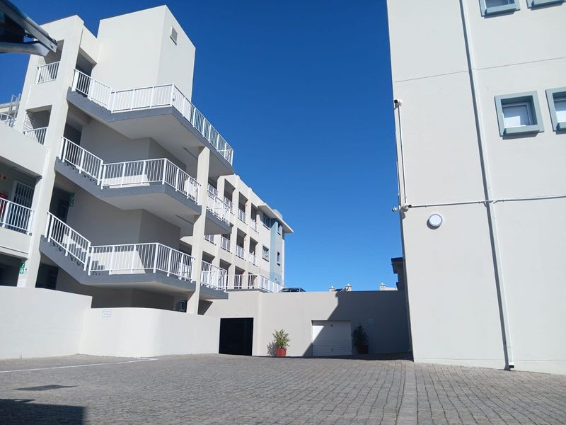 Exterior view of a modern apartment complex featuring a paved driveway, multi-level staircases with white railings, and a garage entrance.