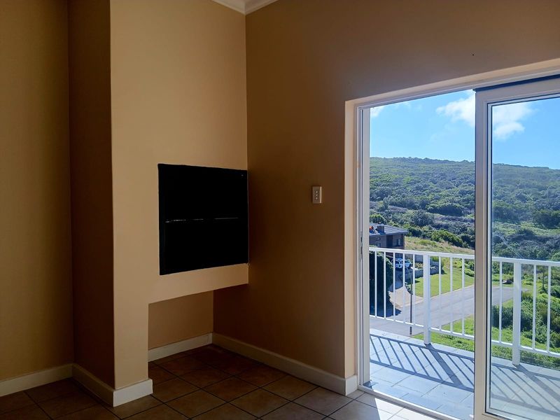 An empty living room featuring a built-in fireplace, tiled flooring, and a sliding glass door leading to a balcony with scenic views.