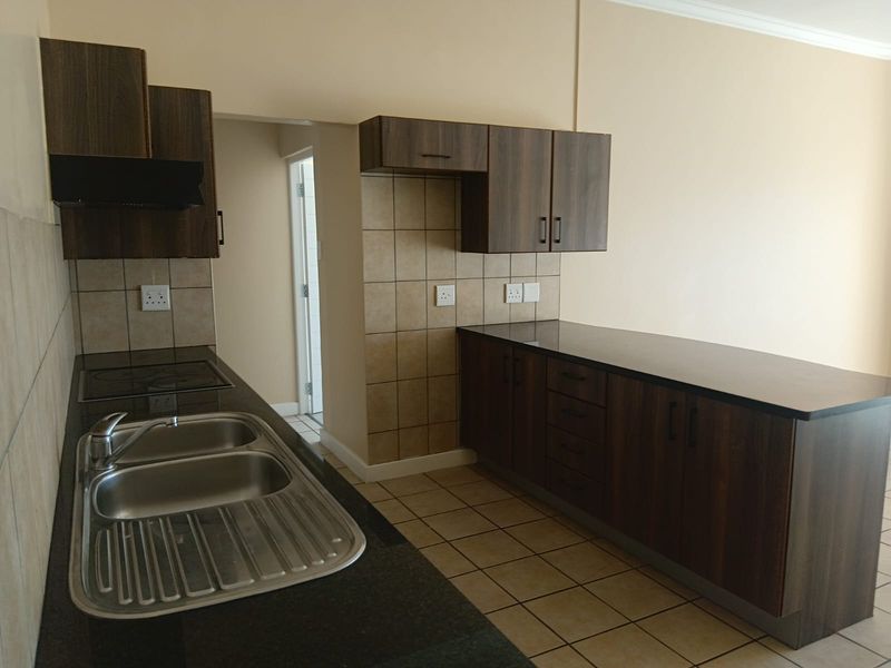 A clean, functional kitchen featuring dark wood cabinetry, granite-look countertops, a double stainless steel sink, and an integrated electric hob with extractor fan.