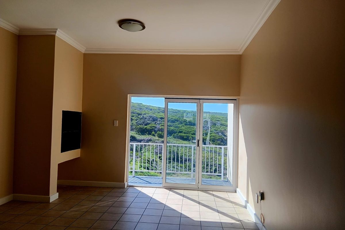 An empty living room featuring tiled floors, a recessed wall niche, and a sliding glass door providing access to a balcony with scenic views.