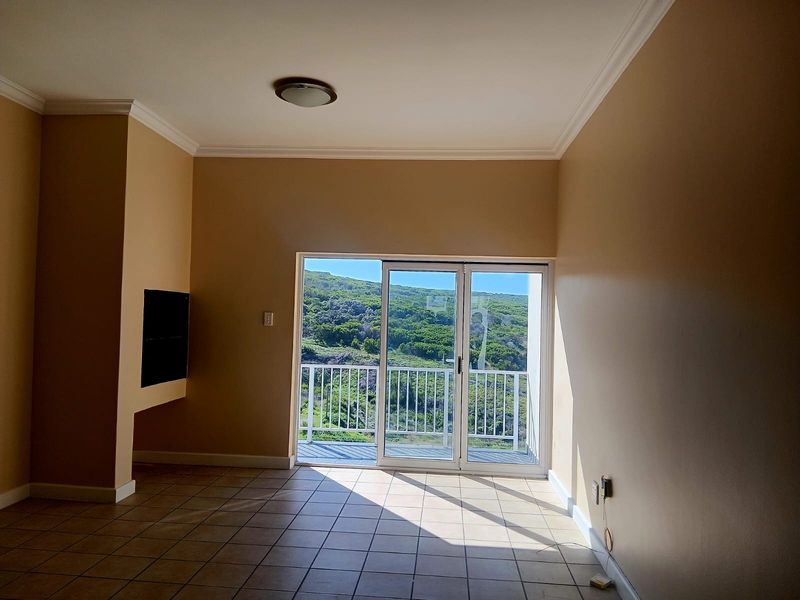 An empty living room featuring tiled floors, a recessed wall niche, and a sliding glass door providing access to a balcony with scenic views.
