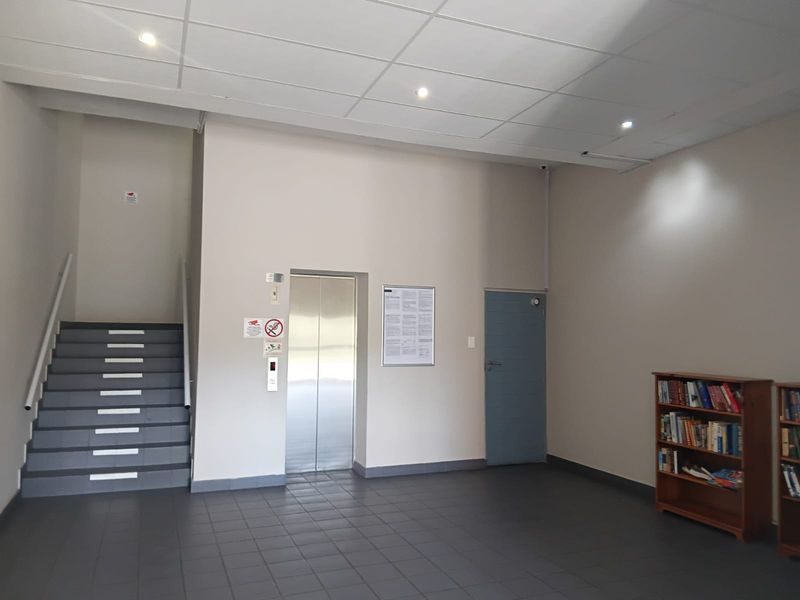 A clean and functional apartment building lobby featuring tiled flooring, a modern elevator, and a staircase providing access to upper levels.
