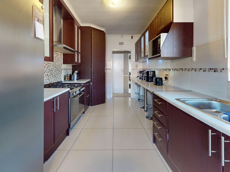 A functional galley-style kitchen featuring dark wood cabinetry, a gas hob with extractor, tiled flooring, and a double sink with a tiled backsplash.