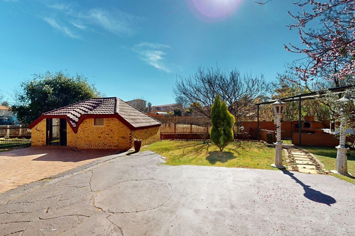 Rear garden area featuring a brick outbuilding, paved driveway with visible cracking, and a dedicated outdoor braai area with a stone pathway.