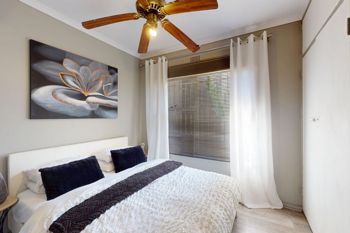 A well-maintained bedroom featuring a ceiling fan, built-in cupboards, and laminate flooring, with natural light provided by a window with venetian blinds.