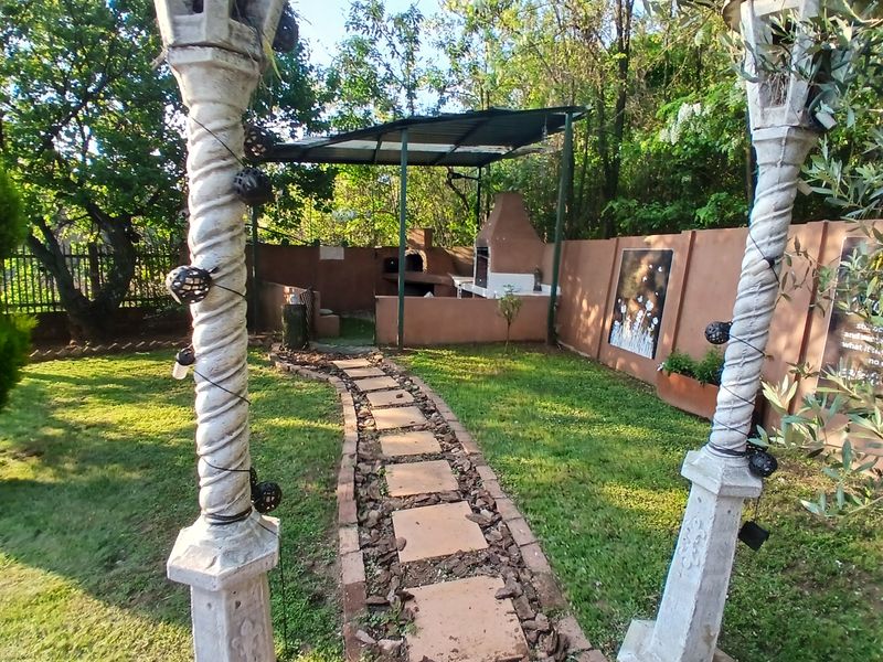 A landscaped garden featuring a stone pathway, decorative pillars, and a built-in outdoor braai area with a covered structure.
