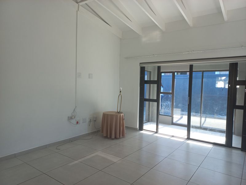A bright, empty living room featuring tiled flooring, exposed beam ceilings, and large sliding glass doors providing access to the exterior.
