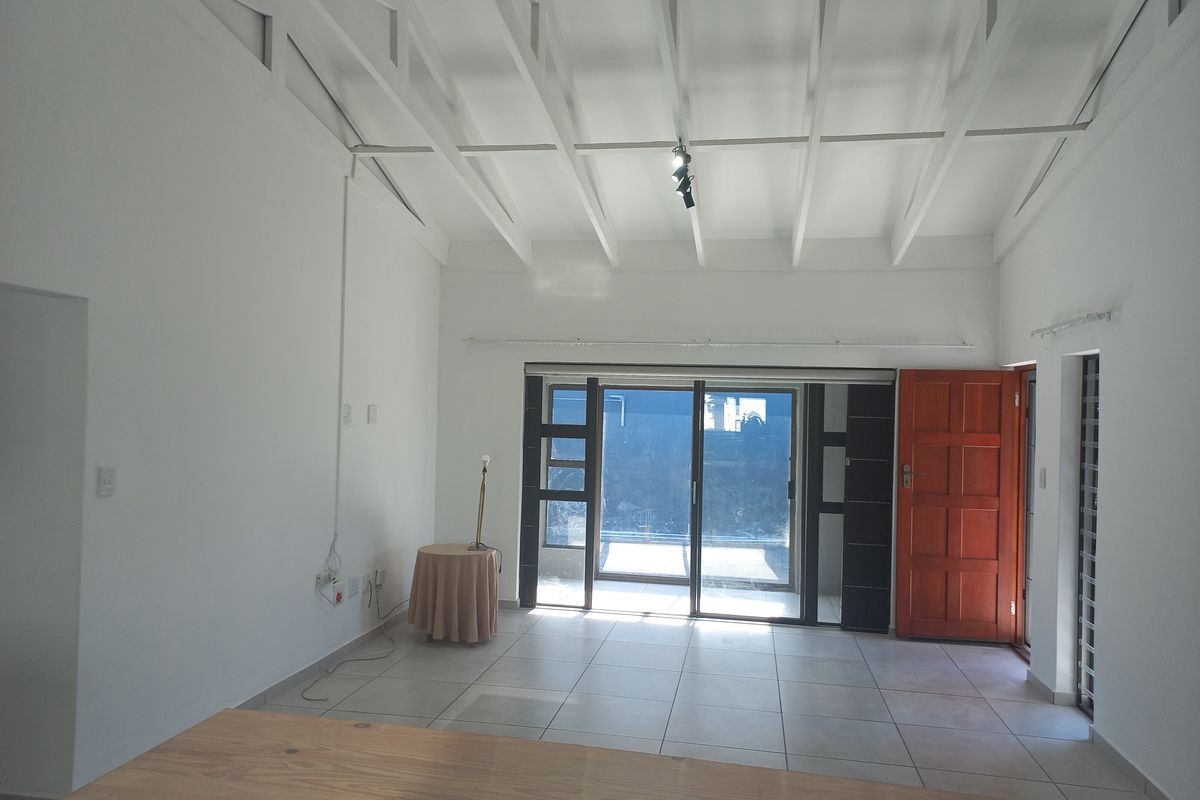 Spacious living area featuring high exposed beam ceilings, neutral tiled flooring, and large sliding glass doors providing ample natural light.