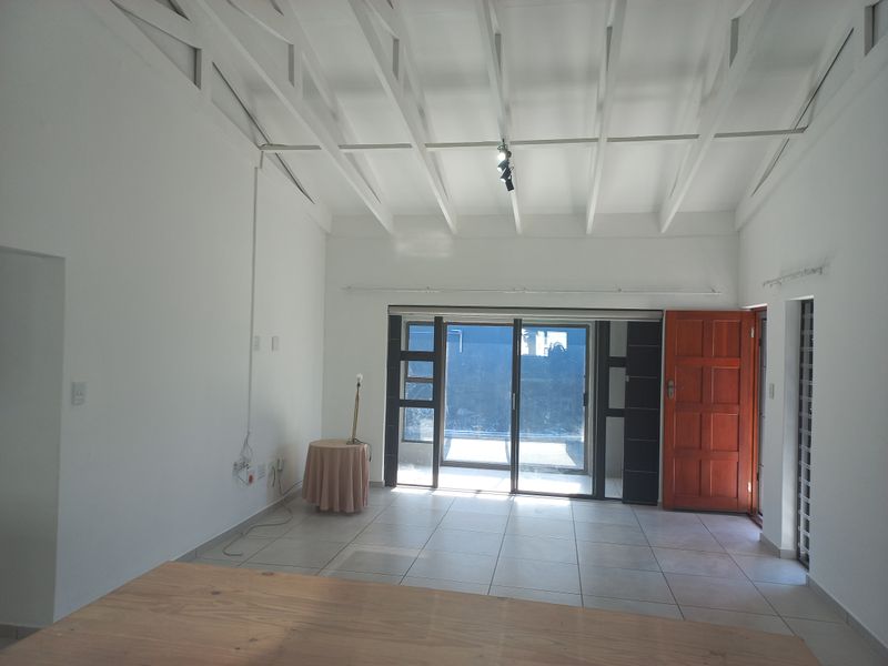 Spacious living area featuring high exposed beam ceilings, neutral tiled flooring, and large sliding glass doors providing ample natural light.