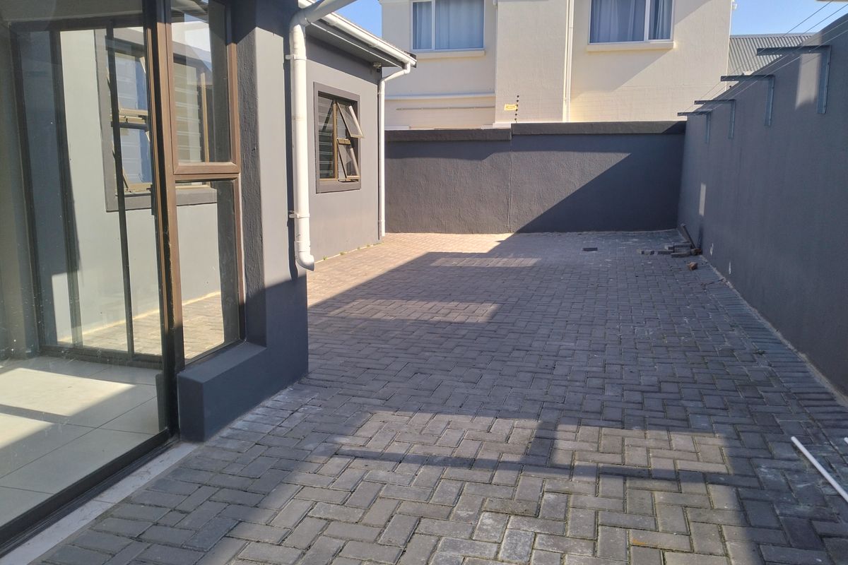 A paved rear courtyard area featuring a boundary wall and access to the interior via a sliding glass door.