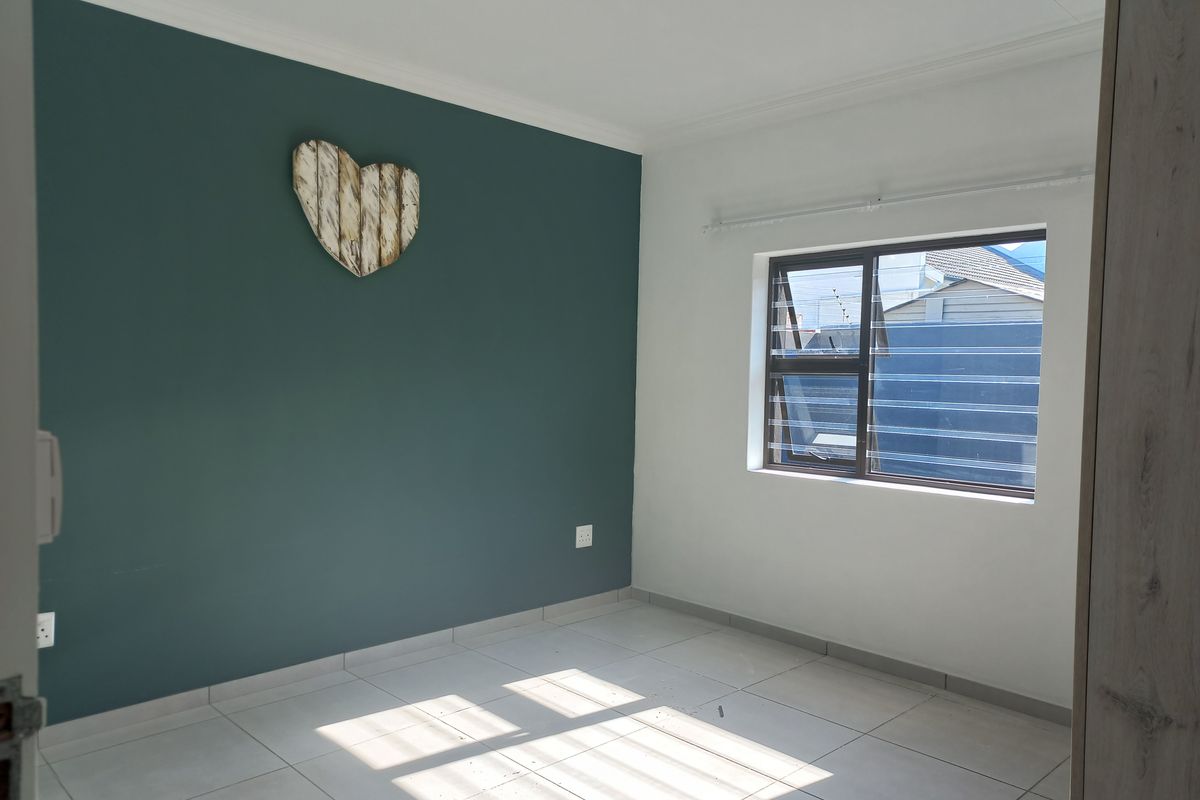 A bright, empty bedroom featuring neutral tiled flooring, a dark teal accent wall, and an aluminium-framed window.