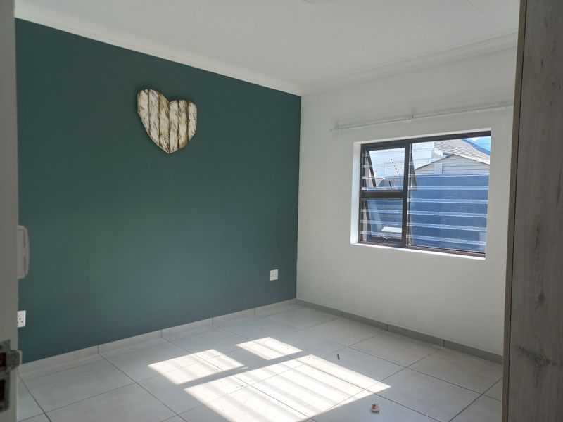 A bright, empty bedroom featuring neutral tiled flooring, a dark teal accent wall, and an aluminium-framed window.
