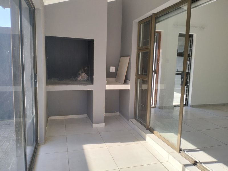 Covered patio area featuring a built-in braai, tiled flooring, and large sliding glass doors providing seamless access to the interior living space.
