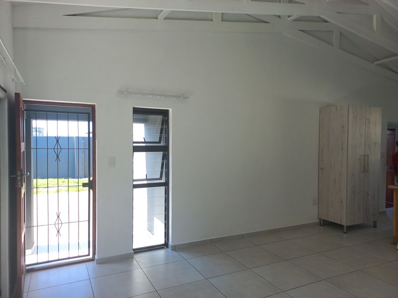 A bright, open-plan living area featuring tiled flooring, exposed white roof trusses, and a secure entrance door with an integrated security gate.