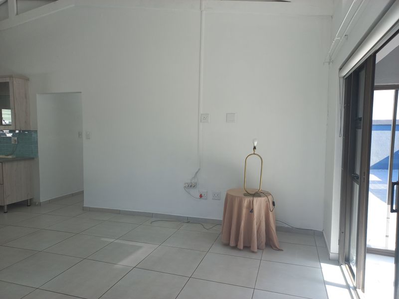 An open-plan living area featuring tiled floors, a sliding glass door to the exterior, and a partial view of the adjacent kitchen area.