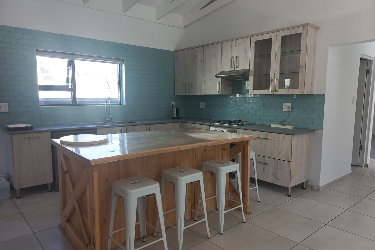 Modern kitchen featuring light wood cabinetry, a central wooden island, blue subway tile backsplash, gas hob, and exposed white ceiling beams.