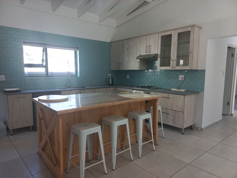 Modern kitchen featuring light wood cabinetry, a central wooden island, blue subway tile backsplash, gas hob, and exposed white ceiling beams.