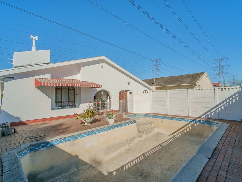 Rear exterior view featuring a paved patio area and an empty swimming pool with perimeter security fencing.