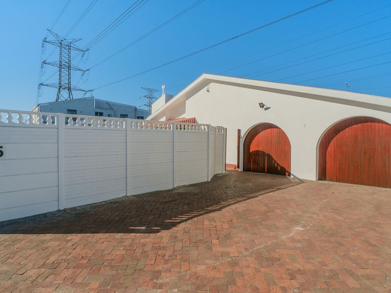 Front exterior view of the property featuring a brick paved driveway, perimeter wall, and two arched garage doors.
